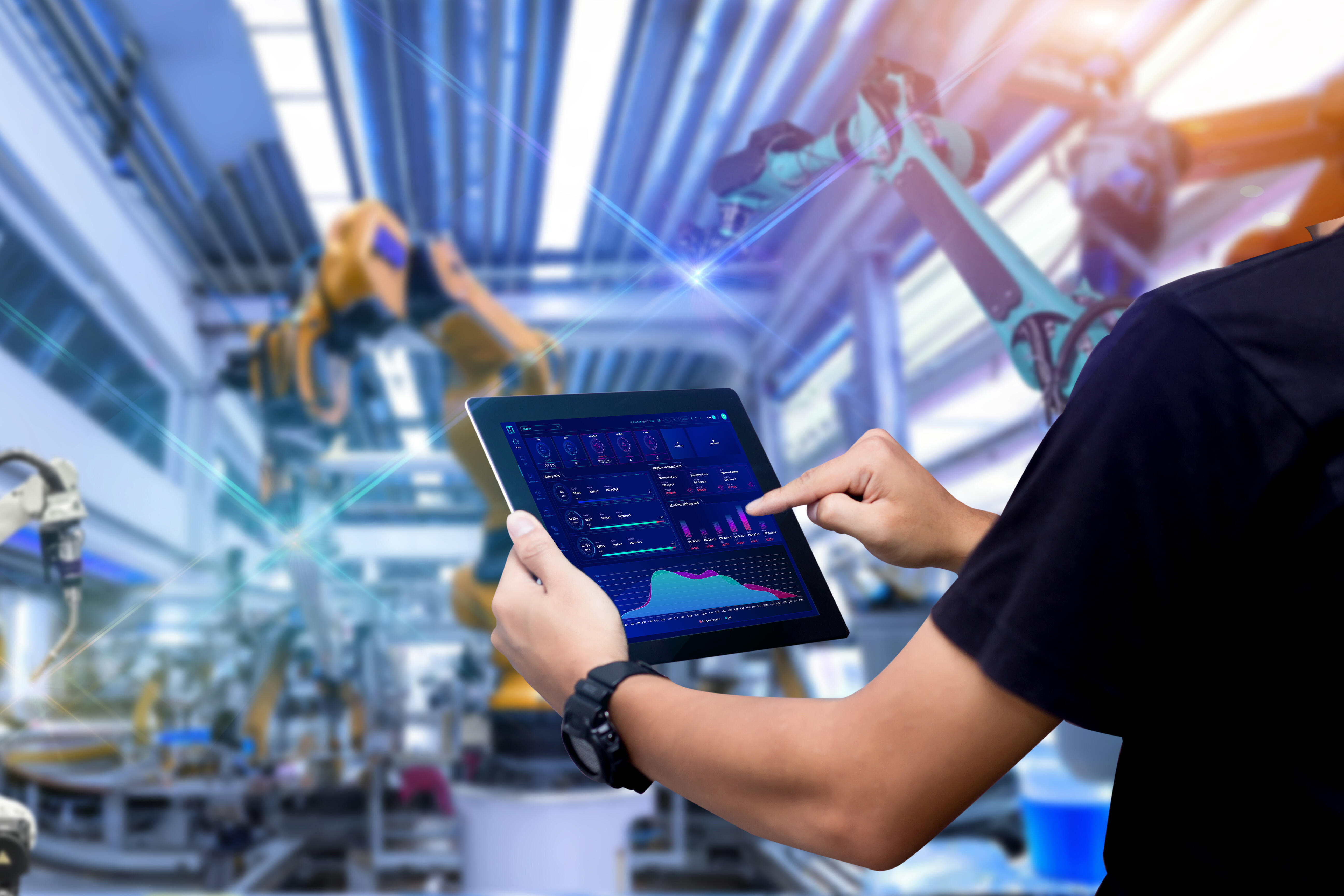 Clouver Dashboard auf Tablet vor einer Halle mit Maschinen