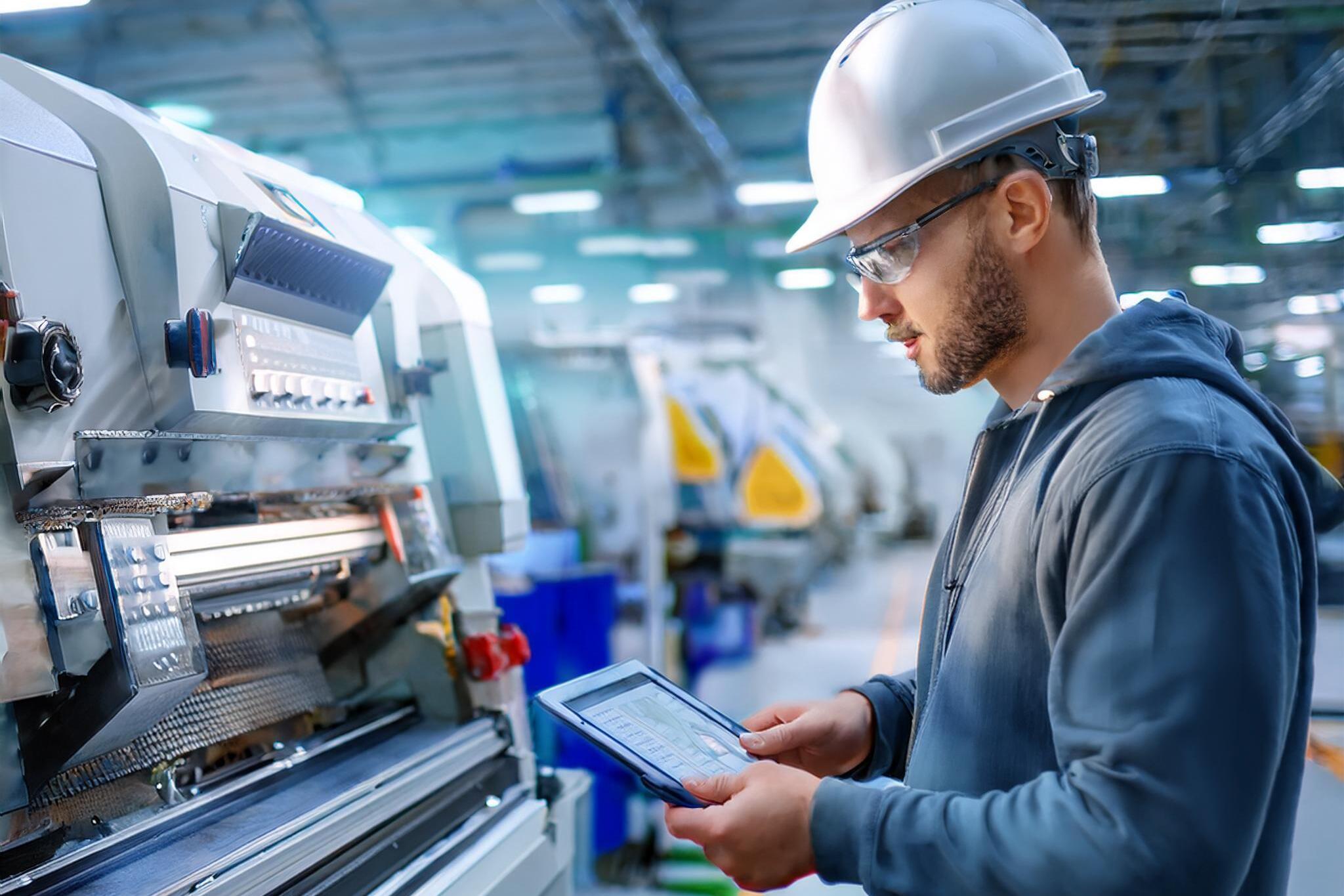 Mann vor Maschine, schaut auf ein Tablet